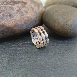 May include: A silver ring with a design of multiple fish, each facing the same direction, encircling the band. The ring is on a dark gray surface.