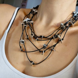 May include: A layered necklace with multiple strands of black cord and silver disc pendants.