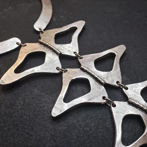 Anatomical silver statement necklace close up on model brick wall, handmade sculptural silver plated geometric necklace chest detail, wearable art jewelry by Gozemre Atelier