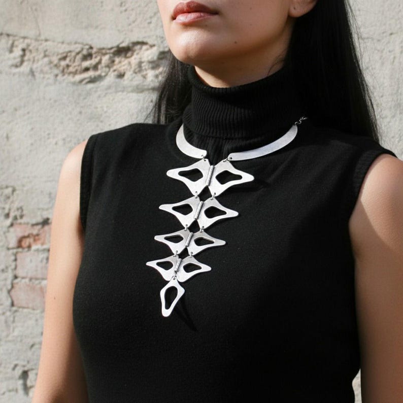 Anatomical silver statement necklace close up on model brick wall, handmade sculptural silver plated geometric necklace chest detail, wearable art jewelry by Gozemre Atelier