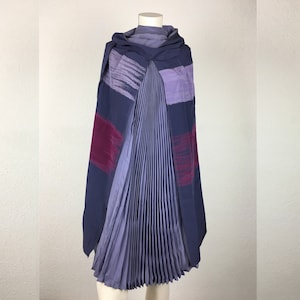 May include: A pleated, purple and burgundy scarf with a geometric pattern. The scarf is draped over a mannequin.