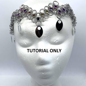 May include: A silver chainmail crown with colourful gemstones and dangling silver teardrop shapes. The crown is on a white mannequin head. "Tutorial Only" is written below the crown.