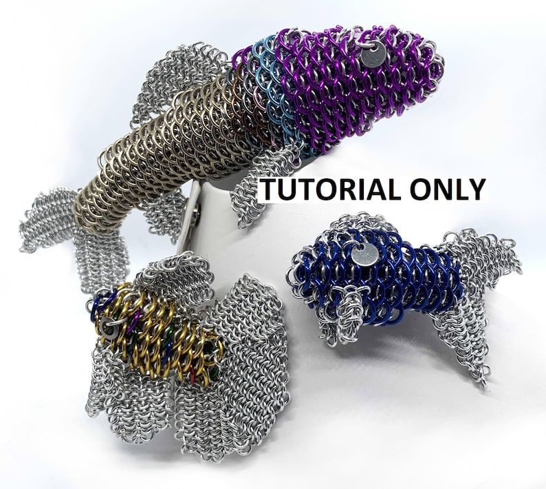 May include: Three silver, blue, and purple chainmail fish sculptures. The fish are made of small metal rings woven together. The fish are on a white surface. "Tutorial Only" is written in black text on the surface.