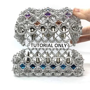 May include: A silver chainmail box with a hinged lid. The box is decorated with blue, purple, and orange gemstones and silver spikes. The box is open and the inside is visible. The text "TUTORIAL ONLY" is printed on the box.