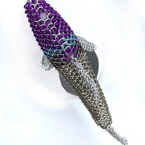 May include: A purple, blue, and silver chainmail fish sculpture. The fish is made of small metal rings that are linked together to create a scale-like effect.