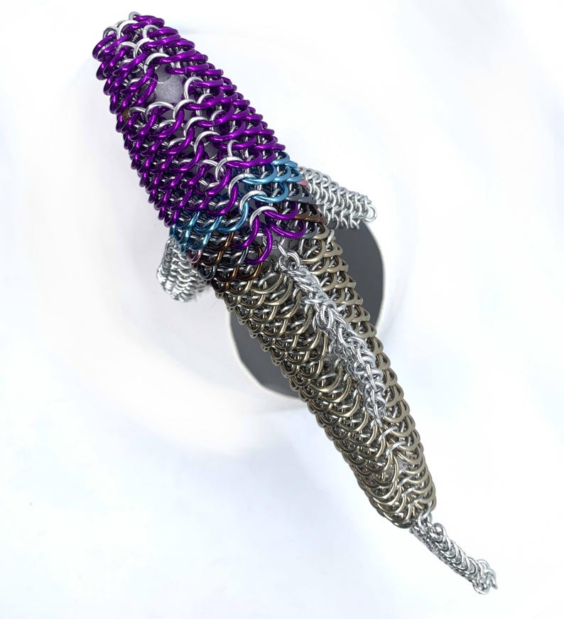 May include: A purple, blue, and silver chainmail fish sculpture. The fish is made of small metal rings that are linked together to create a scale-like effect.