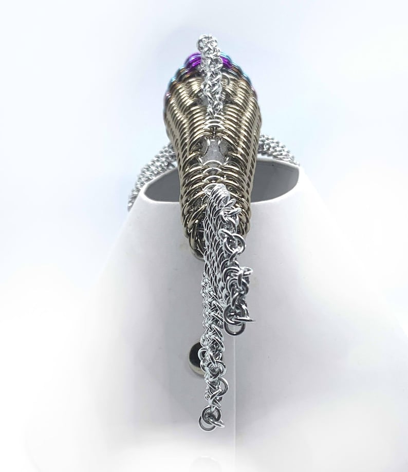 May include: A silver chainmaille necklace with a gold chainmaille pendant. The pendant is decorated with purple and blue beads.