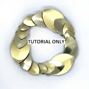May include: A circular bracelet made of overlapping, gold-colored metal scales, connected by small silver rings. The text "TUTORIAL ONLY" is printed in black across the center of the bracelet. The bracelet is set against a white background.