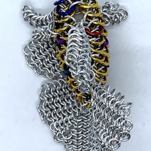 May include: A silver chainmail dragon sculpture with a colorful, multi-layered, gold, green, blue, purple, and red chainmail tail.