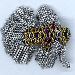 May include: A silver and gold chainmail fish sculpture with colorful accents. The fish has a long, flowing tail and fins.
