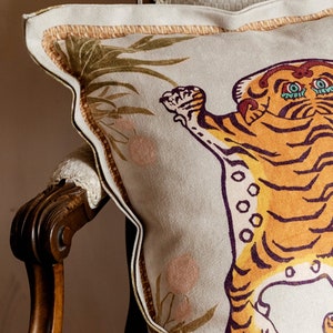 May include: A beige throw pillow with a brown, orange, and purple tiger design. The tiger is standing on its hind legs with its paws raised. The pillow has a brown and beige border.
