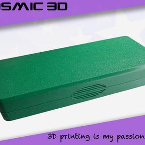 May include: A rectangular, textured, green box with rounded edges. The box has a small, oval-shaped vent on the side. The text "COSMIC 3D" is at the top, and "3D printing is my passion" is at the bottom.