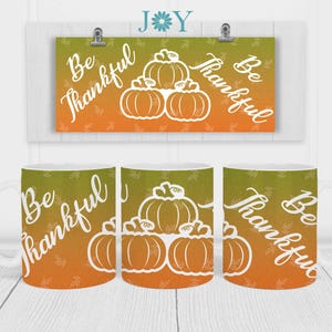 May include: Three white ceramic mugs with a gradient orange and green background. The mugs feature a white outline of pumpkins and the text "Be Thankful".