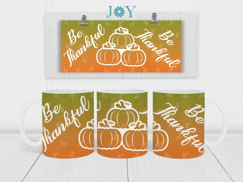May include: Three white ceramic mugs with a gradient orange and green background. The mugs feature a white outline of pumpkins and the text "Be Thankful".