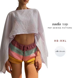 Puede incluir: Un top blanco suelto y unos shorts de ganchillo coloridos. Los shorts presentan rayas horizontales en tonos rosa, verde y amarillo. El texto "nadia top PDF SEWING PATTERN" es visible, junto con las opciones de talla.