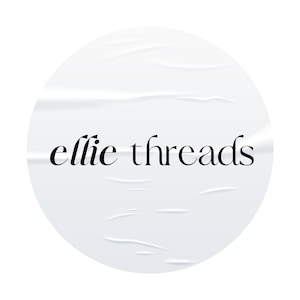 May include: A white, circular sticker with the words "ellie threads" in black script. The sticker has a textured, wrinkled appearance, suggesting it has been applied to a surface. The design is simple and elegant.