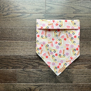 May include: Pink and yellow bandana with a school bus, apple, and rainbow pattern. The bandana has a small tag that says "Sewn by Kim".