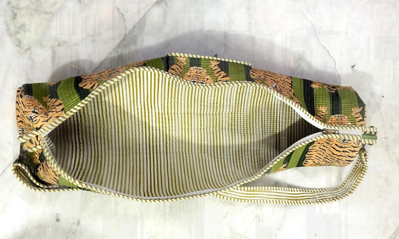 May include: Open, rectangular bag with a tiger print exterior in shades of brown, green, and black. The interior features vertical stripes in light green and white. A white zipper runs along the top edge.