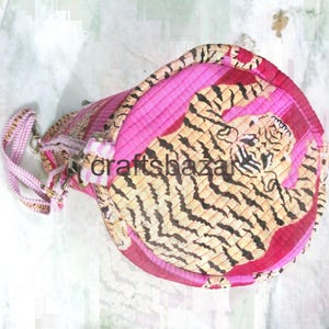 May include: A cylindrical pink and tan handbag with a tiger print design. The bag features a pink strap and zipper closure. The text "craftsbazar" is visible on the side of the bag.