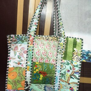 Könnte beinhalten: Eine Patchwork-Tragetasche mit verschiedenen Stoffbahnen mit Blumen- und Mustermotiven in Grün-, Rosa- und Orangetönen. Die Tasche hat ein gestepptes Aussehen mit einem gestreiften Rand und passenden Griffen. Die Tasche ist zum Tragen von Gegenständen konzipiert.
