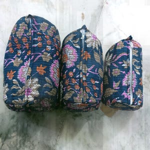 Könnte beinhalten: Drei gesteppte Kosmetiktaschen in verschiedenen Größen. Sie haben einen dunkelblauen Hintergrund mit einem Blumenmuster in Rosa, Braun und Orange. Jede Tasche hat einen weißen Reißverschluss.