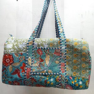 Può includere: Una borsa tote trapuntata con un design patchwork. La borsa presenta una varietà di motivi floreali nei toni del verde acqua, rosso, giallo e verde. I manici sono a righe verde acqua e bianche. La borsa è lunga circa 51 cm.