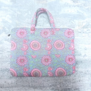 Könnte beinhalten: Eine Tragetasche mit floralem Muster auf grauem Hintergrund. Die Tasche hat ein sich wiederholendes Muster aus rosa Blumen und grünen Blättern auf grauem Hintergrund. Die Griffe sind rosa und die Tasche hat einen Reißverschluss.