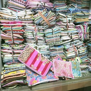 May include: A large collection of colorful, patterned fabric pouches and small bags. The pouches are stacked and bundled, with a variety of designs including stripes, floral prints, and animal patterns. Some are tied with twine or leather straps.