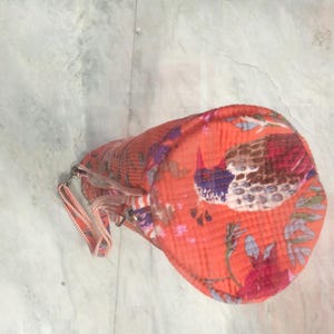 May include: An orange cylindrical bag with a bird and floral pattern. The bag has a zipper closure and a small handle. The bird is depicted with blue, brown, and red colors. The floral pattern includes red and purple flowers.