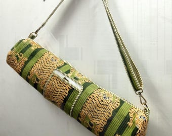 May include: A cylindrical yoga mat bag with a green and tan tiger stripe pattern. The bag has a zipper closure and a matching green and tan shoulder strap. The bag is hanging on a white wall.