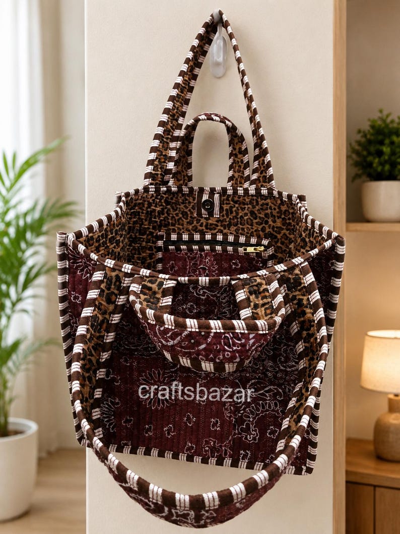 May include: A quilted tote bag featuring a mix of brown and white striped trim, a dark red paisley pattern, and a leopard print interior. The bag has two top handles and a smaller front pocket with the text craftsbazar printed in white.