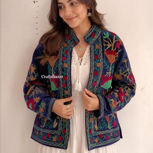 Könnte beinhalten: Eine marineblaue Samtjacke mit lebendiger, mehrfarbiger Blumenstickerei in Rot, Grün und Orange. Die Jacke hat einen Stehkragen, lange Ärmel und ein offenes Vorderteil. Der Text "Craftsbazar" ist auf der Vorderseite der Jacke zu sehen.