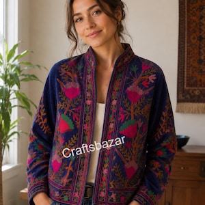 Può includere: Una giacca in velluto blu navy con un vivace motivo floreale ricamato nei toni del rosa, verde e arancione. La giacca presenta un colletto alla coreana, maniche lunghe e un design aperto sul davanti. Il testo "Craftsbazar" è stampato sul davanti.