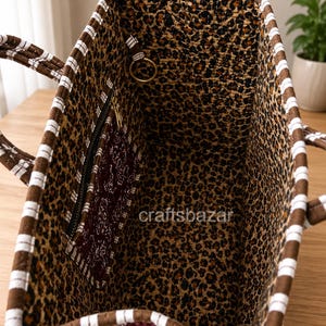 May include: A tote bag with a brown and white striped exterior trim and a leopard print interior lining. The bag features a dark maroon zippered pocket with a white floral pattern and a gold-toned metal ring. The text craftsbazar is visible.