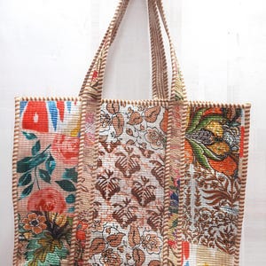 Könnte beinhalten: Eine Patchwork-Tragetasche mit Blumen- und geometrischen Mustern in Rosa, Orange, Braun und Blau. Die Tasche hat zwei Griffe und ist mit einem hellbraunen Stoff verziert. Die Tasche ist aus einem gesteppten Material gefertigt.