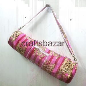 May include: A cylindrical yoga mat bag with a pink and gold tiger stripe pattern. The bag has a matching pink strap and the text "craftsbazar" is visible on the side.