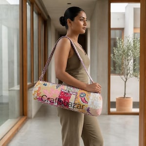 May include: A cylindrical yoga mat bag featuring a patchwork design with floral and bird patterns in shades of pink, yellow, and blue. The bag has a long adjustable shoulder strap and the text Craftsbazar printed on the front surface.