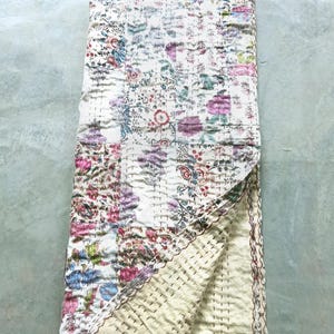 Könnte beinhalten: Eine Steppdecke mit floralem Muster und cremefarbenem Rücken. Die Steppdecke hat ein Patchwork-Design mit verschiedenen Blumen in Rosa-, Lila-, Blau- und Grüntönen. Die Kanten sind mit einem braunen Rand versehen. Die Steppdecke ist gefaltet.