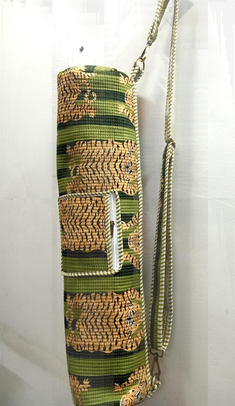 May include: A green and tan yoga mat bag with a tiger print design. The bag has a zippered pocket and a shoulder strap. The bag is cylindrical and made of quilted fabric.