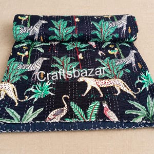 May include: A black quilted throw blanket featuring a repeating pattern of zebras, leopards, and tropical plants in green, white, and yellow. The fabric is stitched with white thread and displays the white text Craftsbazar in the center.