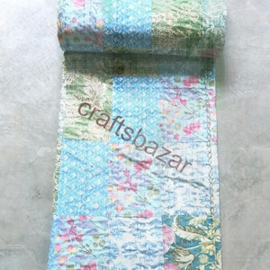 Könnte beinhalten: Eine zusammengerollte Patchwork-Steppdecke mit floralen und gemusterten Stoffen in Blau-, Grün- und Rosatönen. Die Steppdecke hat einen genähten Rand und der Text "craftsbazar" ist auf der Oberfläche sichtbar.