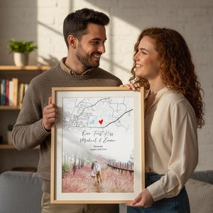 May include: A framed print held by a couple, featuring a map with a red heart marking a location. The print includes the text "Our First Kiss" and the names Michael & Emma, with a date and location.