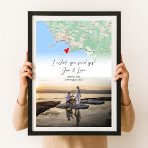 May include: Black framed print featuring a map of Nerano, Italy, with a red heart marker. Text reads "I asked, you said yes!" and names "Jon & Lori." A photograph of a proposal scene is below. The date is 30th August 2025.