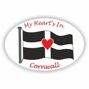 May include: A white oval sticker with a black and white flag of Cornwall with a red heart in the centre. The text "My Heart's In Cornwall" is written in red cursive.