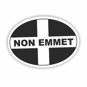 May include: An oval sticker featuring a black background with a white cross. The words "NON EMMET" are printed in bold, black letters across the center of the sticker.