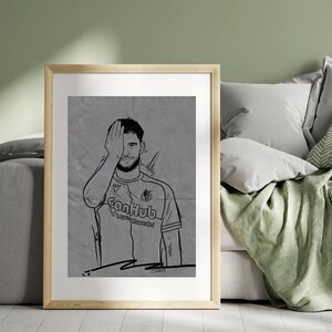 Könnte beinhalten: Ein gerahmter Schwarz-Weiß-Strichdruck einer Person in einem Fußballtrikot, die sich mit der Hand ein Auge bedeckt. Das Trikot trägt den Text "FanHub" und "Loyal Rewarded". Das Kunstwerk ist vor einem grauen Hintergrund.