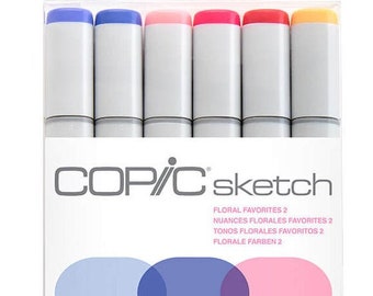 Puede incluir: Un paquete de rotuladores Copic Sketch, Floral Favorites 2. Los rotuladores tienen cuerpos grises y tapas de colores en tonos de azul, rosa, rojo y amarillo. El embalaje incluye el texto "COP/C sketch" y muestras de color.