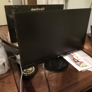May include: Two black computer monitors are displayed on a wooden surface. The monitors have a sleek, rectangular design with a black bezel. The brand name "ViewSonic" is visible on the top of one monitor.