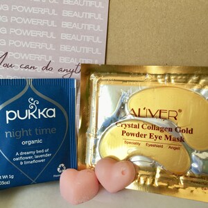 May include: A blue tea bag package with the text "pukka night time organic" and a pink heart-shaped candle. A gold package with the text "ALIVER Crystal Collagen Gold Powder Eye Mask" and two gold eye masks.