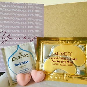 May include: A pink and white cardboard box with the text "You can do anything" printed on it. The box contains two small pink heart-shaped bath bombs, a small white pouch with the text "pukka feel new organic" printed on it, and a gold pouch with the text "ALIVER Crystal Collagen Gold Powder Eye Mask" printed on it.